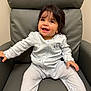 Vanellope is registered to the contest to win money with this photo: baby, child, smiling, happy, sitting, onesie, white_clothing, chair, leather_chair, indoor, cute, portrait, young_child, infant, person, cozy, comfortable, dark_hair, expression, small_hands