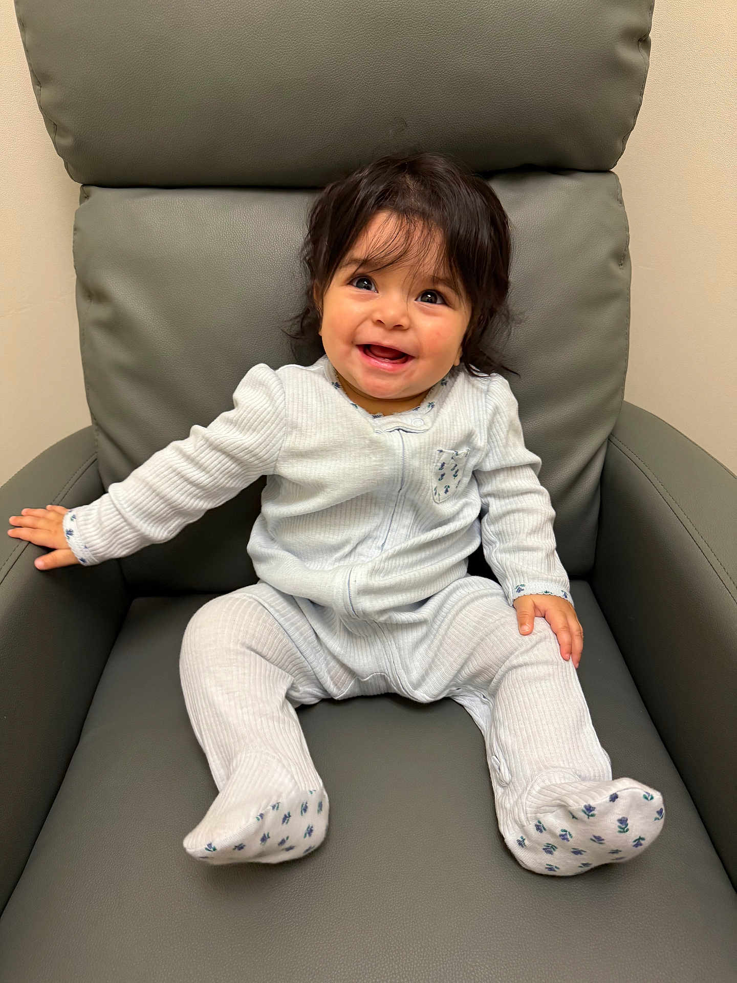 Vanellope is registered to the contest to win money with this photo: baby, child, smiling, sitting, onesie, white_clothing, indoor, chair, leather, happy, cute, infant, portrait, young_child, small_hands, small_feet, dark_hair, cozy, comfortable, expression