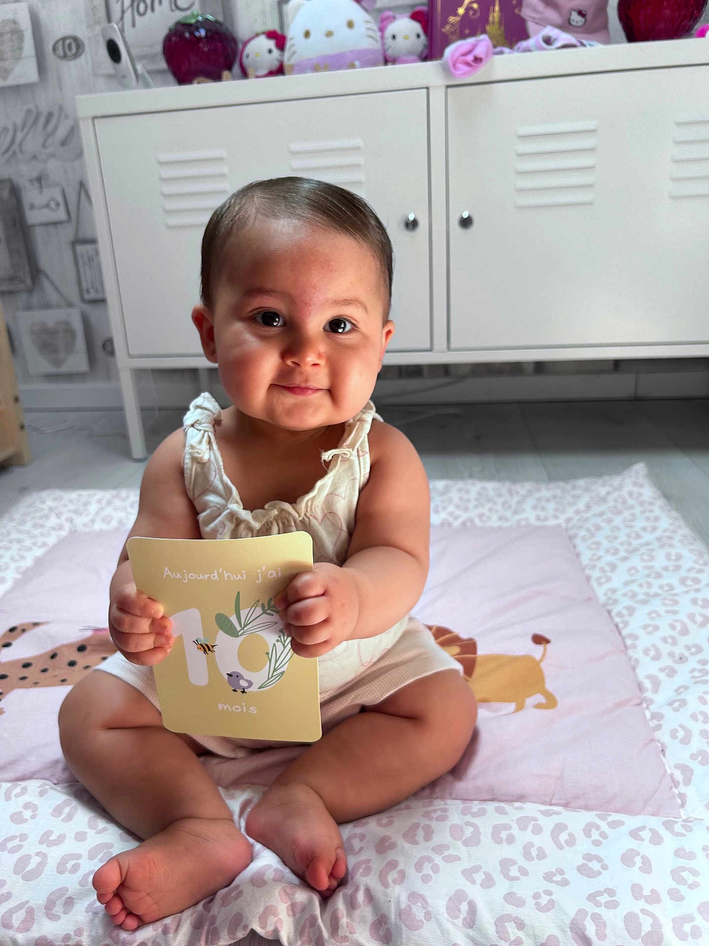 Aliyah participe au concours pour gagner de l'argent avec cette photo : baby, infant, milestone_card, sitting, cute, nursery, soft_toy, plush, floor_mat, child, indoors, smiling, portrait, clothing, hands, feet, face, decor, room, person