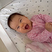 Talia joined the competition — help win amazing prizes! baby, infant, crib, smiling, laughing, pink_clothing, onesie, blanket, star_pattern, moon_pattern, mattress, bed, happy, cute, child, face, indoors, soft_toys, sleepwear, resting