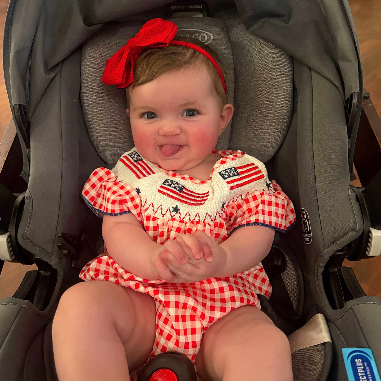 Abby joined the competition — help win amazing prizes! baby, child, car_seat, red_bow, tongue_out, smiling, cheeks, clothing, red_white_checkered, american_flag, headband, indoor, seat_belt, infant, cute, playful, person, portrait, happy, baby_girl