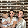 Elyo participe au concours pour gagner de l'argent avec cette photo : baby, woman, people, portrait, smile, brick_wall, tattoo, watch, bracelet, earrings, necklace, striped_clothing, white_clothing, holding, indoor, casual, happy, family, person, young