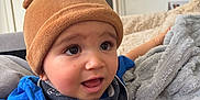 Elyo a rejoint le concours — aidez-le/la à gagner de superbes lots ! baby, blanket, blue_shirt, child, clothing, comfort, couch, cozy, curious, expression, face, hat, headwear, home, indoor, person, scarf, seated, soft_texture, young_child