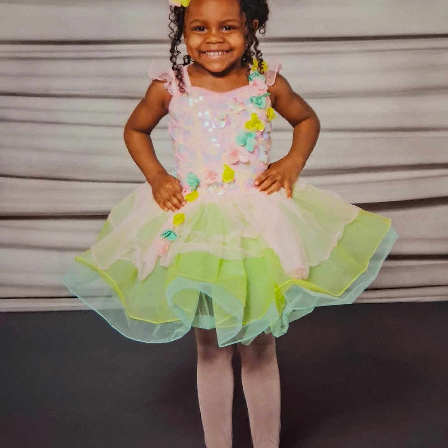 Layla is registered to the contest to win money with this photo: child, girl, smiling, dress, colorful, tutu, posing, happy, curly_hair, flower_hair_accessory, tights, ballet_shoes, studio, portrait, standing, confident, cute, fashion, young, background
