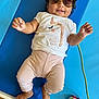 baby, child, sunglasses, unicorn, shirt, pink_pants, blue_mat, toy_car, smiling, lying_down, indoor, cute, happy, person, feet, hand, curly_hair, playtime, casual_clothing, infant
