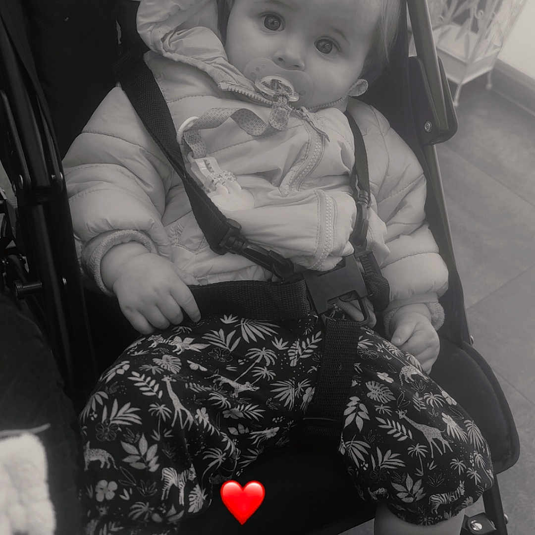 Célina-Marie a rejoint le concours — aidez-le/la à gagner de superbes lots ! toddler, child, stroller, jacket, pacifier, pants, patterned_pants, sitting, indoor, floor, baby, cute, face, expression, footwear, socks, seatbelt, black_and_white, heart_emoji, curious