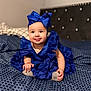 baby, child, blue_dress, headband, bow, bedspread, pattern, happy, smiling, tongue_out, sitting, indoor, cute, infant, hands, feet, soft_focus, bed, fabric, portrait