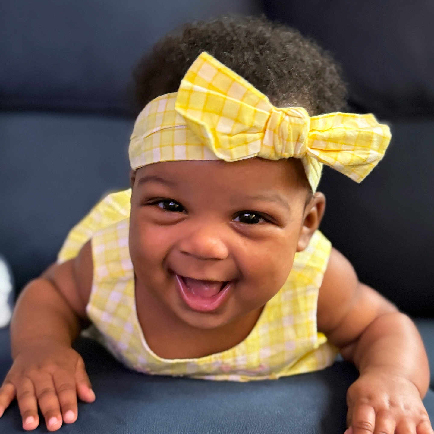 Aleiyah joined the competition — help win amazing prizes! baby, smiling, yellow_headband, yellow_bow, yellow_dress, infant, happy, cute, child, portrait, face, hands, couch, blue_cushion, indoors, closeup, skin, hair, expression, toddler