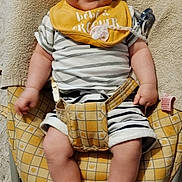 Hélios a rejoint le concours — aidez-le/la à gagner de superbes lots ! baby, baby_chair, bib, child, comfort, face, footwear, happy, indoor, infant, pacifier, patterned_fabric, person, plush, seated, smiling, striped, striped_clothing, toddler, yellow