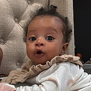Amari joined the competition — help win amazing prizes! baby, infant, child, face, eyes, clothing, pajamas, fabric, cushion, chair, curly_hair, expression, cute, indoors, portrait, skin, hand, lying_down, soft_lighting, cozy