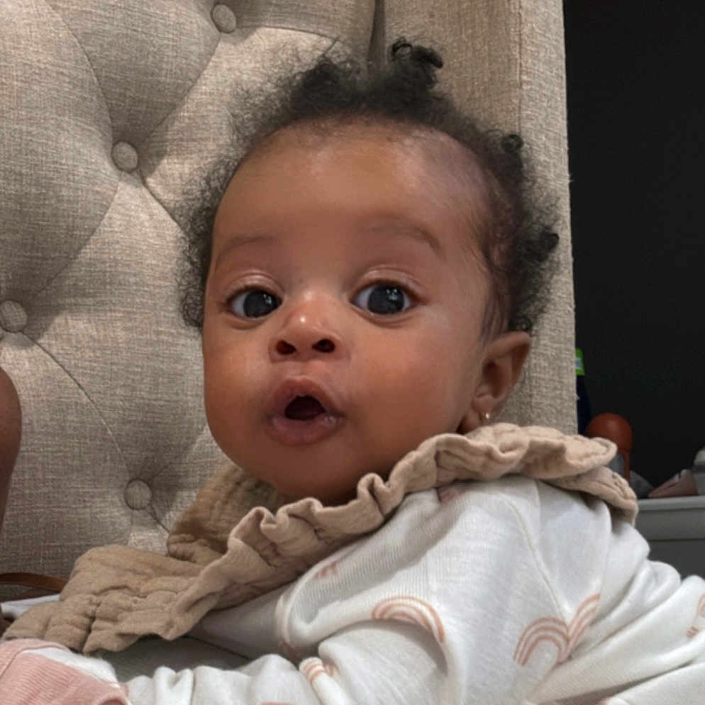 Amari joined the competition — help win amazing prizes! baby, chair, child, clothing, cozy, curly_hair, cushion, cute, expression, eyes, fabric, face, hand, indoors, infant, lying_down, pajamas, portrait, skin, soft_lighting