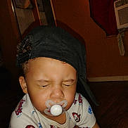 Raymason is registered to the contest to win money with this photo: baby, black_cap, cap, cap_backwards, child, clothing, cute, expression, floor, headwear, indoor, kid, pacifier, person, shirt, spiderman, squinting, toddler, wooden_floor, young_child