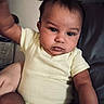 baby, child, infant, onesie, couch, arm, face, eyes, hand, skin, hair, indoors, person, portrait, sitting, wall_decor, photograph, furniture, expression, closeup