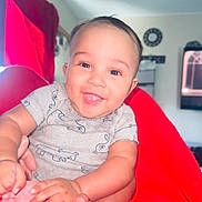 Kylo is registered to the contest to win money with this photo: baby, smiling, tongue_out, red_blanket, indoor, cute, child, happy, infant, clothing, person, face, head, skin, hand, foot, cozy, bright, portrait, seated