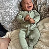 baby, infant, smile, green_onesie, blanket, pillow, floral_pattern, happy, lying_down, cute, child, cozy, soft_texture, indoors, portrait, face, hand, foot, sleepwear, relaxed