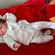 élyne a rejoint le concours — aidez-le/la à gagner de superbes lots ! baby, infant, white_sweater, white_pants, red_blanket, pillow, lying_down, indoors, cozy, soft_fabric, cute, small_hands, face, head, newborn, child, resting, blanket, warm, comfort