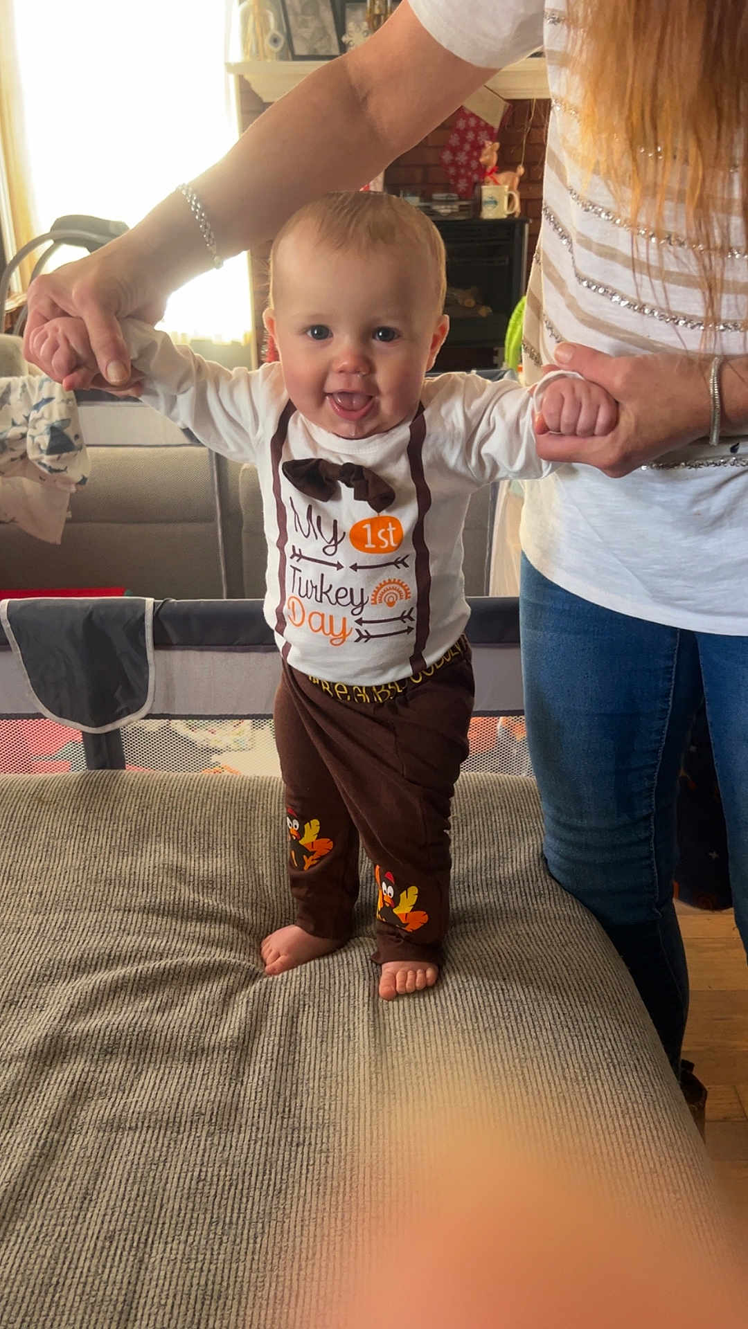 Damon is registered to the contest to win money with this photo: adult, baby, barefoot, child, clothing, couch, cute, footwear, happy, holding_hands, holiday, home, indoor, living_room, pants, person, shirt, smiling, standing, thanksgiving