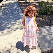 Kyla is registered to the contest to win money with this photo: child, girl, curly_hair, dress, flower, sidewalk, shadow, outdoor, sunlight, plants, tree, concrete, nature, summer, casual, happy, portrait, standing, daytime, playful