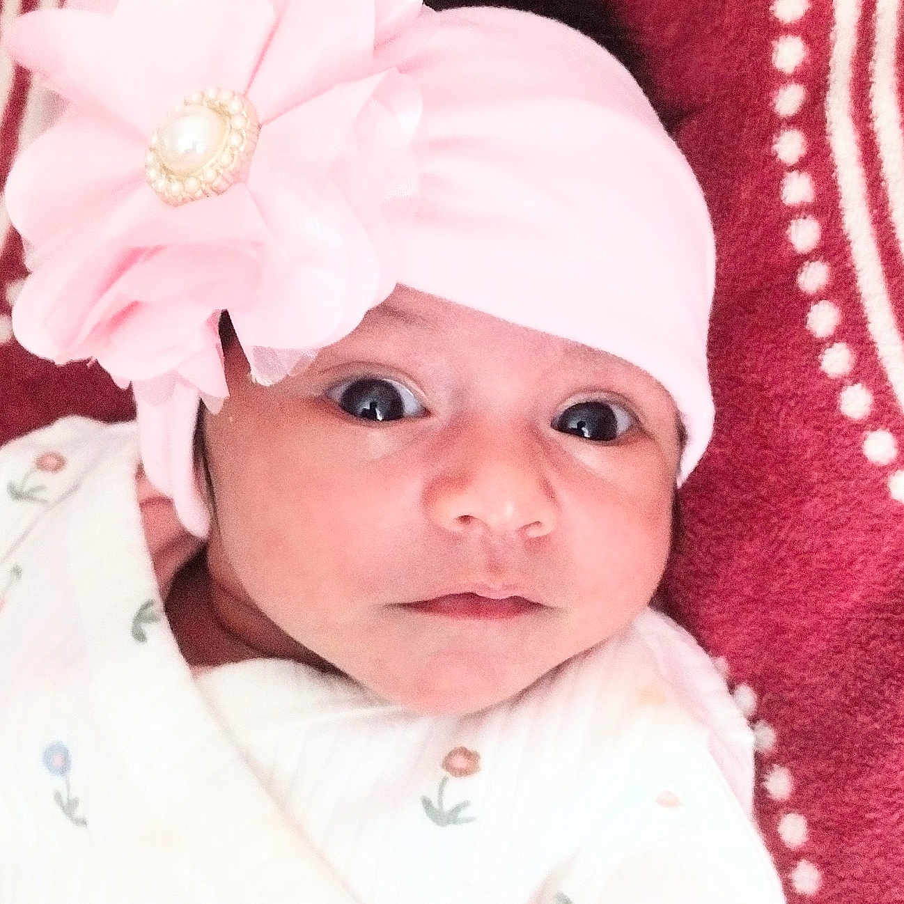 Seerat Kaur is registered to the contest to win money with this photo: baby, blanket, child, close_up, clothing, cute, eyes, face, floral, flower, headband, indoor, infant, looking_at_camera, lying_down, onesie, photography, pink, portrait, textile