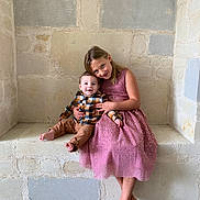 Nolan a rejoint le concours — aidez-le/la à gagner de superbes lots ! child, baby, siblings, girl, boy, dress, plaid_shirt, stone_wall, bench, smile, barefoot, portrait, indoor, cute, happy, family, hug, seated, rustic, cozy