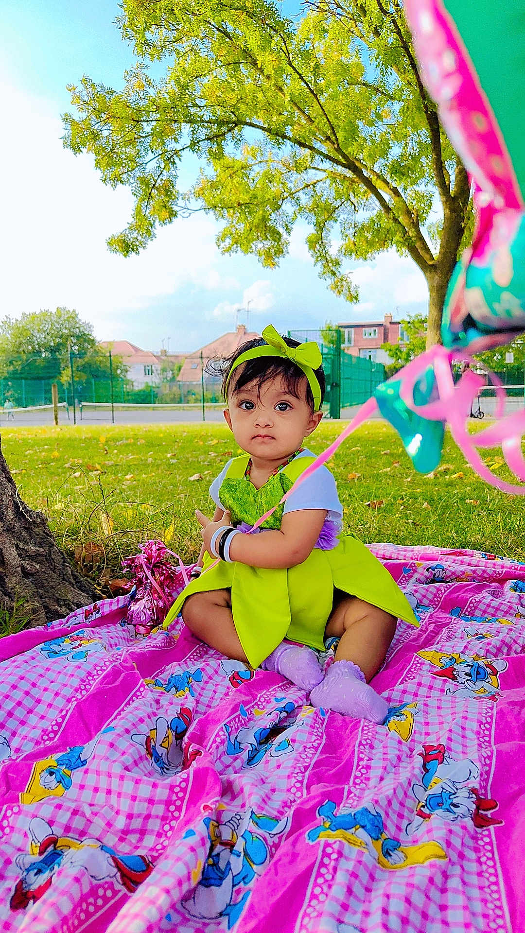 Luvella is registered to the contest to win money with this photo: toddler, child, baby, outdoor, park, grass, tree, blanket, balloons, dress, headband, purple_socks, colorful, sunny, nature, sitting, cute, young_child, playful, daytime