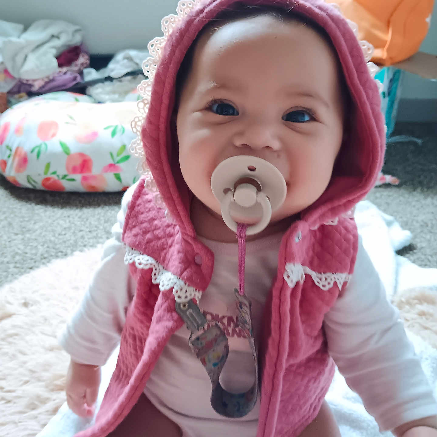 Mckinley joined the competition — help win amazing prizes! baby, blanket, blue_eyes, carpet, child, clothing, cute, diaper, face, homedecor, indoor, infant, lace_trim, pacifier, person, pink_hood, sitting, smiling, soft_toys, vest