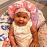 baby, child, smiling, pink_bonnet, onesie, blanket, hand, happy, infant, cute, indoors, portrait, person, skin, face, expression, seated, colorful, soft, cozy