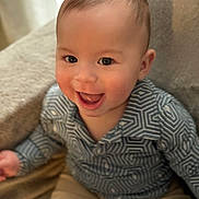 Jeremias joined the competition — help win amazing prizes! baby, child, smile, happy, sitting, face, clothing, patterned_shirt, shorts, indoors, soft_surface, cute, portrait, infant, joyful, human, young_child, eyes, skin, hair