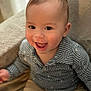 baby, child, smile, happy, sitting, face, clothing, patterned_shirt, shorts, indoors, soft_surface, cute, portrait, infant, joyful, human, young_child, eyes, skin, hair