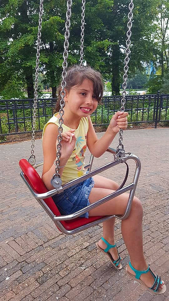 Celia participe au concours pour gagner de l'argent avec cette photo : child, fun, girl, joy, leg, leisure, outdoor_play_equipment, person, play, playground, public_space, recreation, sitting, smile, summer, swing, toddler, tree, vacation