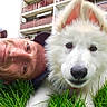 man, dog, white_dog, grass, outdoor, building, balcony, face, pet, animal, close_up, portrait, fluffy, ears, nose, head, smile, casual, hat, nature