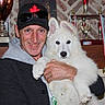 man, dog, white_dog, trophy, medal, ribbon, cap, sunglasses, smile, indoor, shelf, award, portrait, pet, holding, proud, fluffy, animal, person, celebration