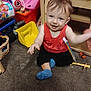 toddler, child, smiling, indoor, carpet, toy, colorful, red_shirt, blue_socks, sitting, happy, face, hand, playroom, plastic_toy, basket, furniture, floor, baby, cute