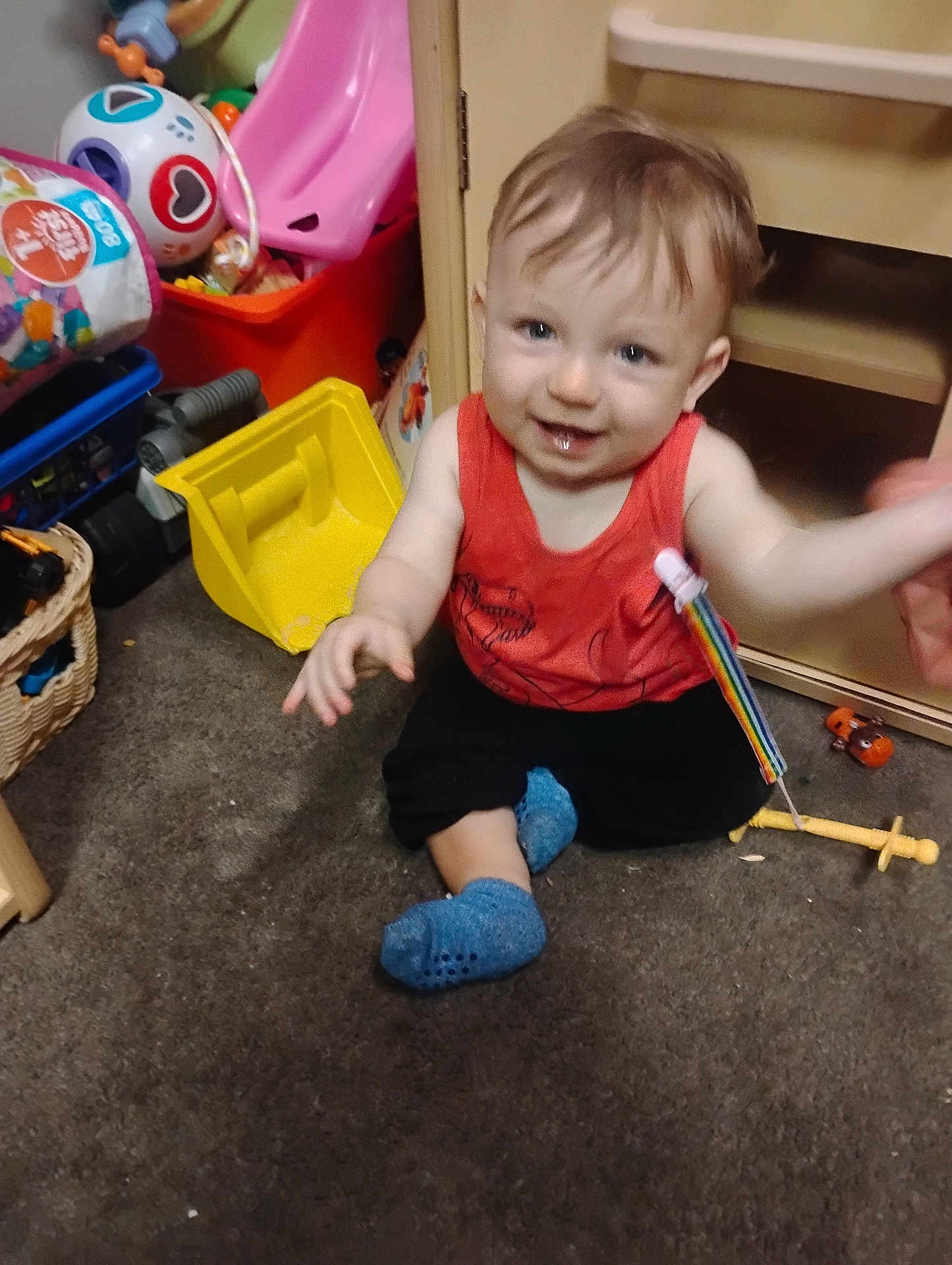 Arkadian joined the competition — help win amazing prizes! toddler, child, smiling, indoor, carpet, toy, colorful, red_shirt, blue_socks, sitting, happy, face, hand, playroom, plastic_toy, basket, furniture, floor, baby, cute