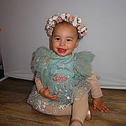 Francesca is registered to the contest to win money with this photo: toddler, child, smiling, dress, flower_crown, green_dress, sitting, wooden_floor, happy, portrait, cute, indoor, fashion, party, young_child, footwear, golden_shoes, long_sleeves, baby, playful