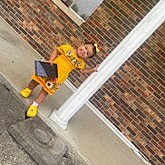 Cattleya Gómez joined the competition — help win amazing prizes! baby, bow, brick_wall, child, clothing, column, concrete, footwear, happy, headwear, outdoor, pacifier, person, porch, smiling, standing, tablet, toddler, yellow_dress, yellow_shoes