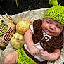 baby, infant, knitted_hat, green_hat, crocheted_vest, onions, wooden_sign, shrek, warning_sign, beige_blanket, outdoor, portrait, cute, baby_clothing, hand, face, eyes, smile, baby_boy, nature