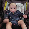 baby, infant, child, car_seat, portrait, sitting, serious_expression, face, eyes, hands, legs, clothing, patterned_outfit, socks, automobile, safety_labels, padded_seat, stuffed_animals, indoor, photography