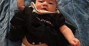 Harmony is registered to the contest to win money with this photo: baby, infant, child, portrait, lying_down, blue_blanket, pink_bow, headband, black_outfit, diaper, remote_control, indoor, closeup, face, eyes_open, fist, arms, legs, textile, adorable