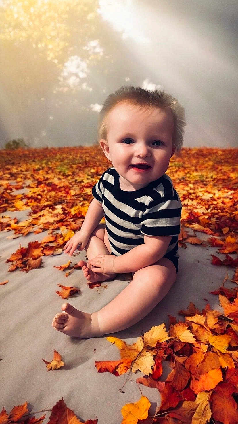 Noah is registered to the contest to win money with this photo: baby, clothing, dress, face, flower, grass, head, leaf, nature, outdoors, pants, person, photography, plant, portrait, rock, sitting, sky, tree, vegetation