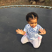 Omarianna is registered to the contest to win money with this photo: toddler, child, trampoline, outdoor, yard, leaves, logs, tree, clothing, smile, happy, sitting, person, play, casual, nature, sunlight, short_hair, footwear, fun