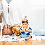 Simeon joined the competition — help win amazing prizes! baby, birthday, party_hat, balloons, wooden_floor, decorations, blue_clothing, smiling, celebration, child, infant, sitting, one_year_old, party, cute, festive, floor, toy, indoor, photography