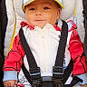 Logan a rejoint le concours — aidez-le/la à gagner de superbes lots ! baby, child, stroller, cap, hat, red_clothing, white_clothing, harness, happy, smiling, infant, cute, face, portrait, outdoor, seat, comfort, babywear, small_person, casual
