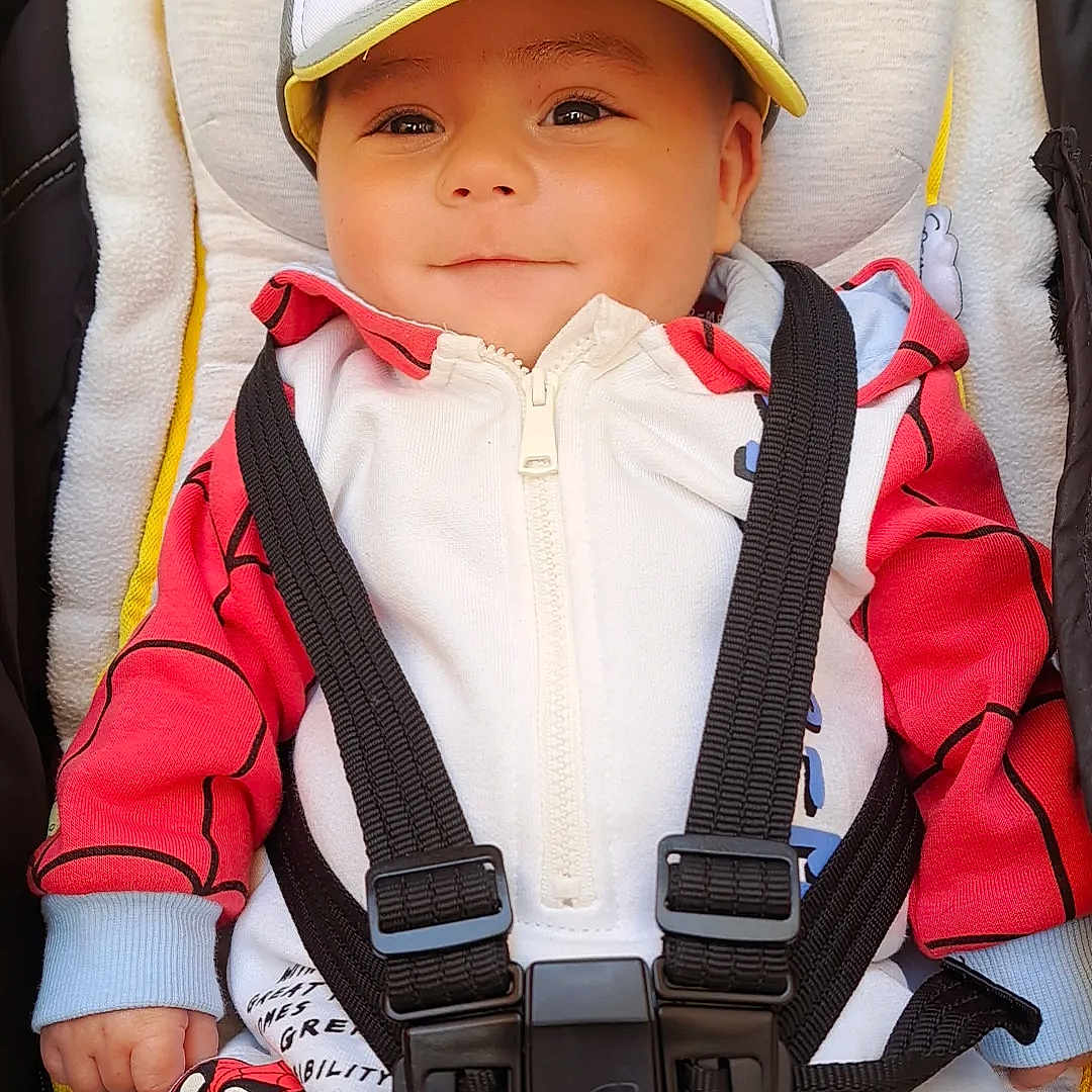 Logan a rejoint le concours — aidez-le/la à gagner de superbes lots ! baby, child, stroller, cap, hat, red_clothing, white_clothing, harness, happy, smiling, infant, cute, face, portrait, outdoor, seat, comfort, babywear, small_person, casual