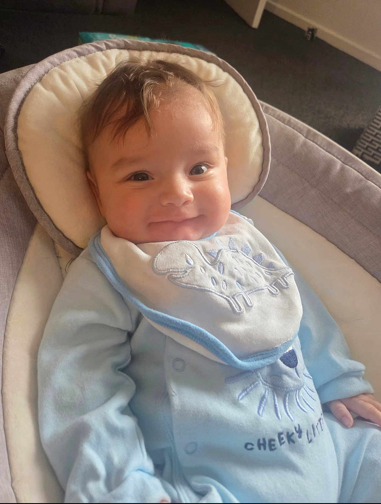 Jace joined the competition — help win amazing prizes! baby, infant, smile, onesie, bib, dinosaur, cushion, baby_seat, indoor, child, clothing, face, happy, cute, soft_lighting, young_child, portrait, relaxing, cozy, human