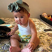 Halo is registered to the contest to win money with this photo: baby, child, infant, headband, bow, white_tank_top, bed, quilt, floral_pattern, foot, hand, curious, indoor, toy, remote_control, sitting, skin, cute, people, person