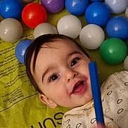 Amal is registered to the contest to win money with this photo: baby, child, smiling, play_mat, colorful_balls, toy, indoor, happy, person, infant, cute, closeup, face, clothing, patterned_outfit, hand, play_area, bright_colors, young_child, lying_down