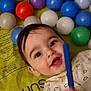 baby, child, smiling, play_mat, colorful_balls, toy, indoor, happy, person, infant, cute, closeup, face, clothing, patterned_outfit, hand, play_area, bright_colors, young_child, lying_down