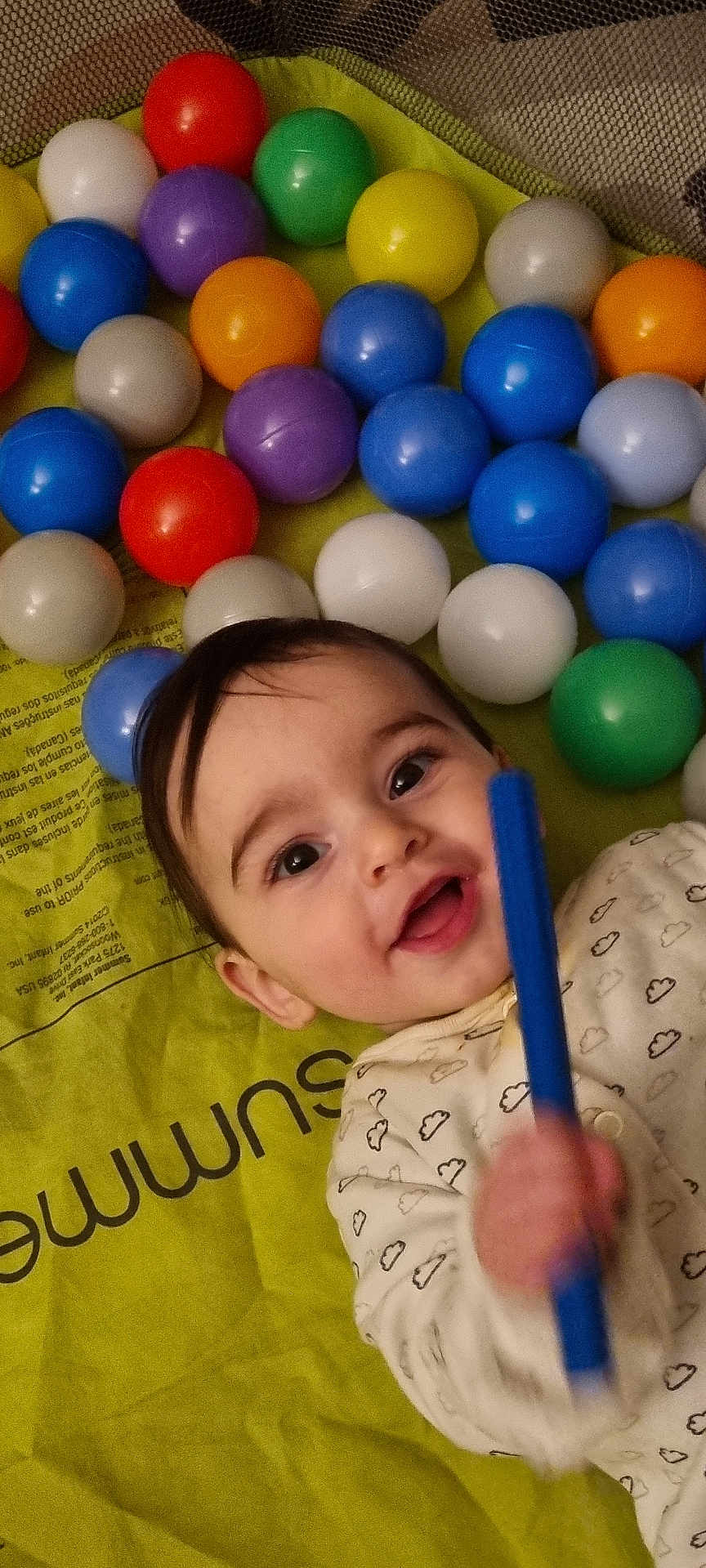 Amal is registered to the contest to win money with this photo: baby, child, smiling, play_mat, colorful_balls, toy, indoor, happy, person, infant, cute, closeup, face, clothing, patterned_outfit, hand, play_area, bright_colors, young_child, lying_down