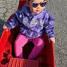 child, toddler, sunglasses, purple_hoodie, pink_leggings, red_wagon, outdoor, sunlight, pavement, toy, play, casual_clothing, cute, sitting, young_child, fashion, fun, daytime, person, accessory